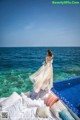 A woman in a long dress standing on the edge of a swimming pool.