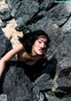 A naked woman laying on a rock on the beach.