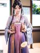 A woman in a purple and white dress holding a fan.