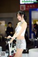 A woman standing next to a bike on display.