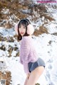 A woman in a pink sweater and ear muffs posing in the snow.