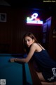 A woman sitting at a pool table in a dark room.